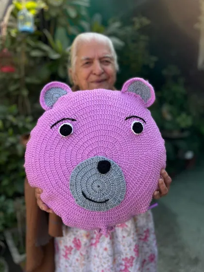 A friendly purple bear cushion to brighten up your space. This round pillow is soft, huggable, and full of handmade charm.