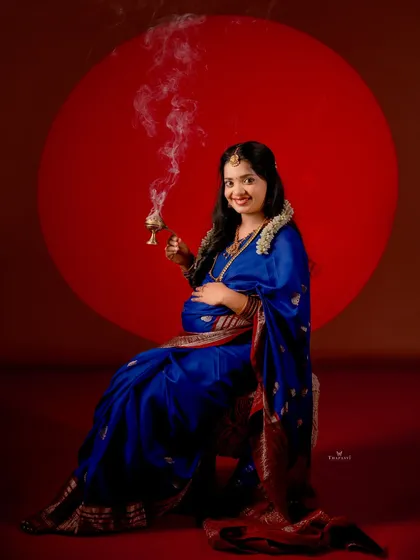 Looking directly at the camera, this portrait captures the confidence and joy of the mother-to-be in her royal blue saree, holding a traditional dhuni.