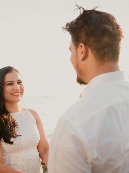An over-the-shoulder shot capturing the bride's beautiful smile as she looks at her partner. The golden hour lighting on the beach adds a warm, romantic glow.