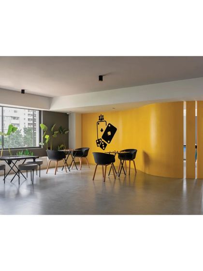 A curved yellow wall defines the card room and lounge area in the 'Meraki' clubhouse. This element adds a soft, organic shape to the otherwise rectilinear space.