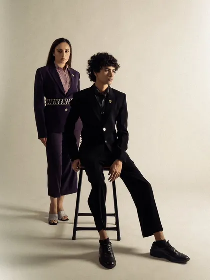 A full-length shot of two models in tailored suits, showcasing the brand's range. The clean studio setting and formal posing create a sophisticated and professional look.
