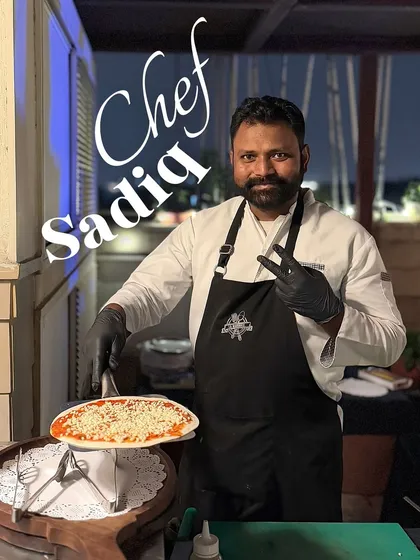 This is Chef Sadiq, one of our pizza specialists. Here he is at an outdoor event, proudly presenting a freshly made cheese pizza, ready for the oven.