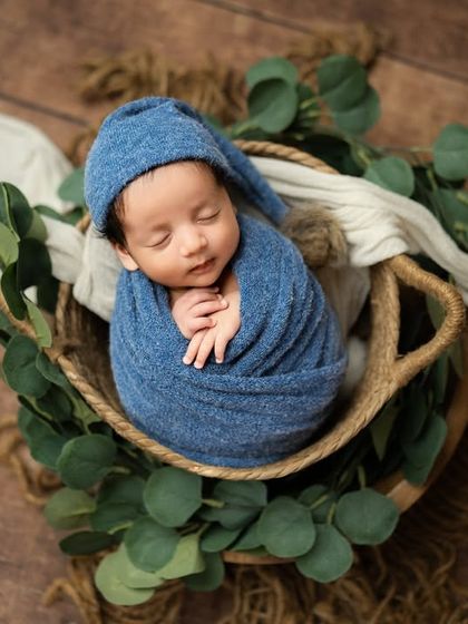An overhead shot of a baby boy nestled in a basket adorned with eucalyptus leaves. The combination of deep blue and natural green is both calming and beautiful.