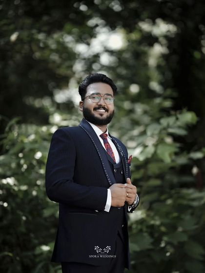 A handsome portrait of the groom in his suit, looking happy and relaxed against a backdrop of lush greenery.