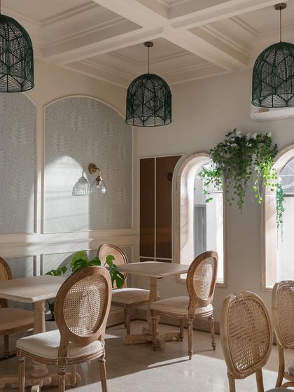 A bright, sunlit corner of a cafe project, featuring cane-backed chairs and delicate wallpaper. This space was designed to feel light, airy, and elegant.