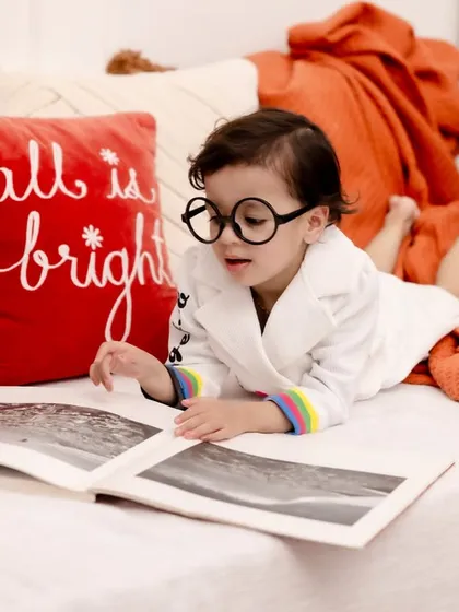 Starting the story of a lifetime. This cozy "little bookworm" setup, complete with a comfy bed and glasses, is a charming way to capture a child's curious spirit.