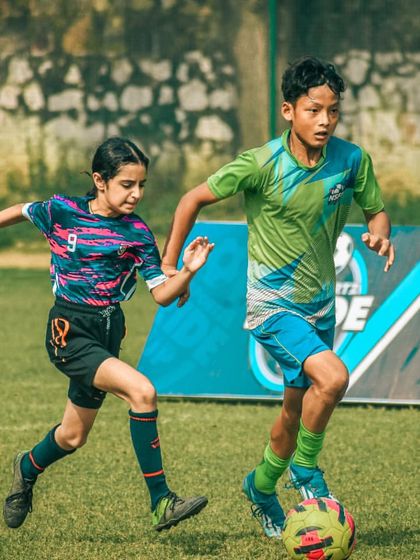 A female player dribbles the ball while a male player defends, highlighting our inclusive co-ed training environment.