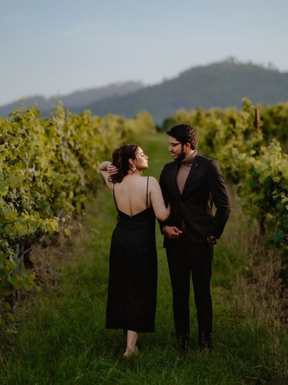 A beautiful, candid-style shot of a couple walking through a vineyard in Thailand. The woman's glance back at the camera adds a touch of playful connection to this romantic scene.
