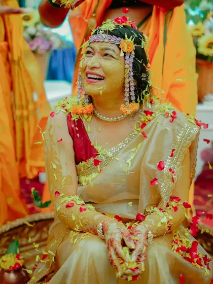 The bride's face is full of joy as she is showered with turmeric and flower petals by her loved ones.
