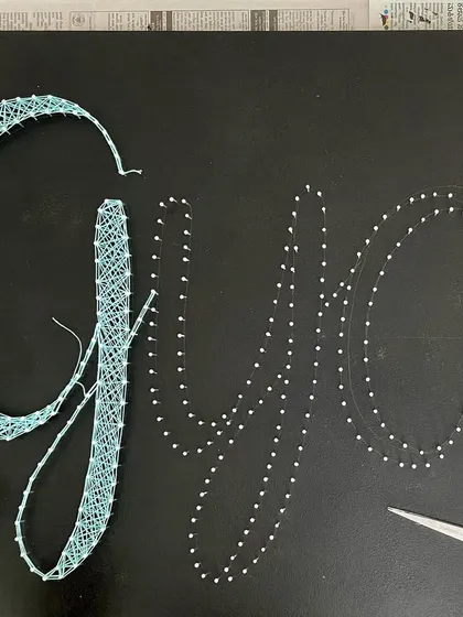 A close-up of the string art name board, showing the nails and the beginning of the weaving process.