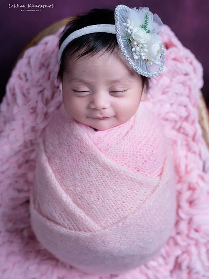 A beautiful, classic portrait of an 8-day-old baby girl, snugly wrapped in pink with a delicate headband, showcasing a sweet, sleepy smile.