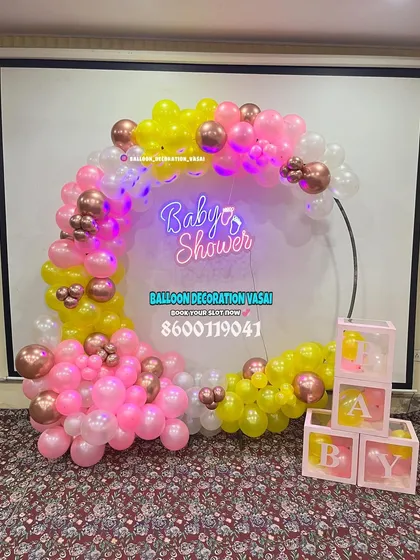 A modern ring backdrop is a great choice for smaller spaces. This baby shower setup uses a vibrant mix of pink and yellow balloons, a neon sign, and transparent "BABY" blocks for a trendy look.