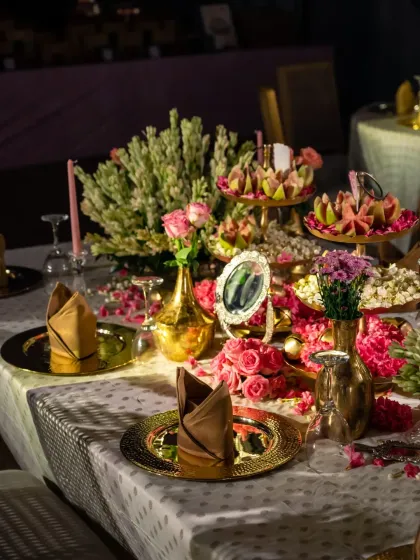 An intricate and beautifully styled table setting, featuring gold plates, fresh flowers, and traditional sweets.