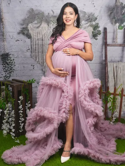 A full-length studio portrait showing off a beautiful dusty pink ruffled gown with a high slit. This style is perfect for highlighting your baby bump while adding a touch of glamour and sophistication to your maternity photos.