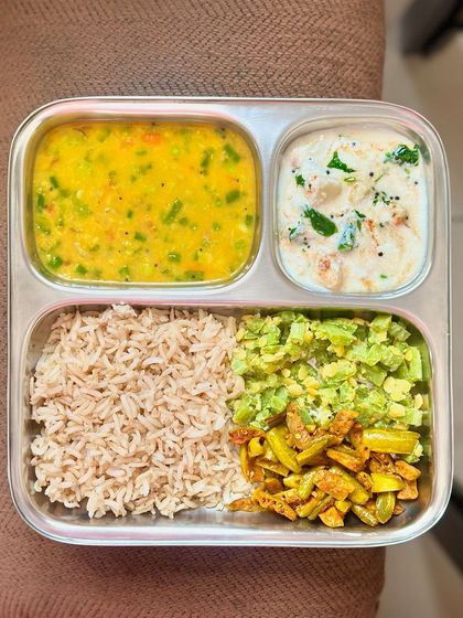 A colorful and balanced plate of brown rice, mixed vegetable dal, sautéed snake gourd and ivy gourd, and a refreshing raita.