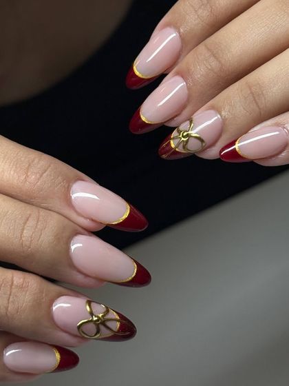 A sophisticated and festive French manicure with a twist. This design features a deep red tip outlined in gold, with two accent nails adorned with 3D gold bow charms.