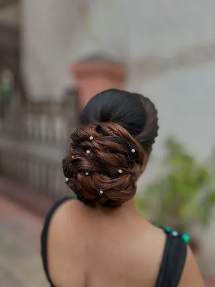 An elegant and intricate low bun hairstyle, adorned with small pearls. This is a classic look for receptions and parties.