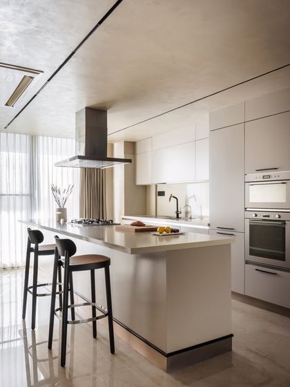 The kitchen is designed for simplicity and function, featuring a clean white island with a built-in cooktop and breakfast bar. The handleless cabinetry and integrated appliances maintain the minimalist aesthetic that defines the entire penthouse.