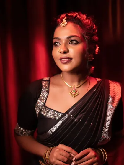 A model posing in a black saree, with dramatic lighting that highlights her features.