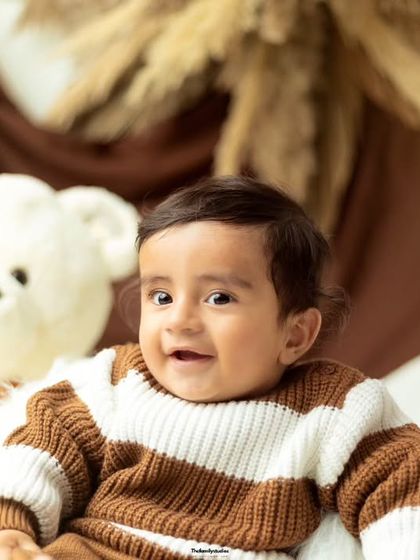 A gentle smile from a baby boy during his sitter session, captured in a warm, brown-toned studio setup.