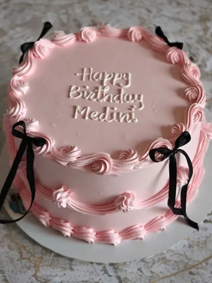 A vintage-style pink cake with delicate piping and black ribbons. This "coquette" style is very trendy and adds a touch of classic elegance.