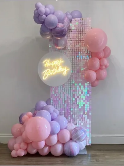 A beautiful pastel balloon arrangement on an iridescent shimmer panel. The soft pink and purple balloons combined with the "Happy Birthday" neon sign create a soft, magical look.