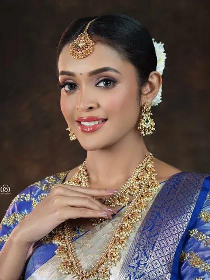 A close-up beauty shot focusing on the model's joyful expression and the detailed bridal jewelry. The soft lighting and traditional attire create a classic and timeless portrait.