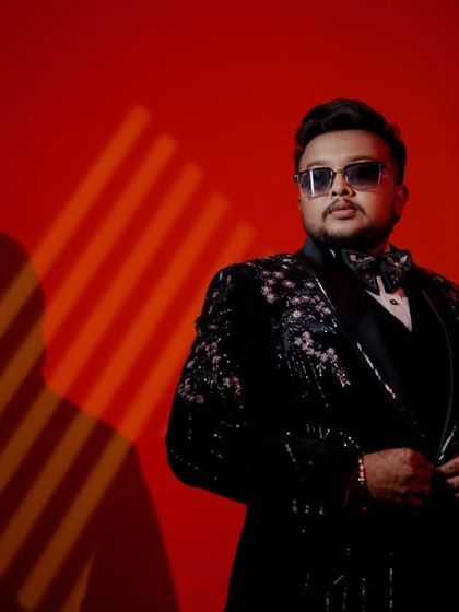 A dramatic portrait of the groom in his reception suit, set against a bold red background.