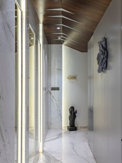 Modern elegance graces this passageway in the Filigree House. The combination of white marble floors, dramatic lighting, and a sculptural wooden ceiling creates a dynamic and sophisticated journey through the home.