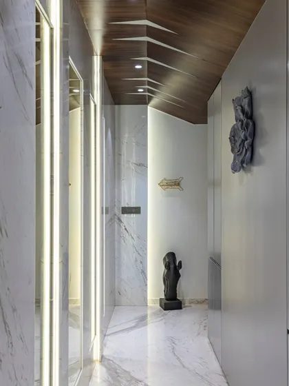Modern elegance graces this passageway in the Filigree House. The combination of white marble floors, dramatic lighting, and a sculptural wooden ceiling creates a dynamic and sophisticated journey through the home.