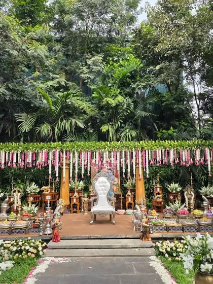 An outdoor puberty ceremony setup that blends with the natural garden surroundings. I created a floral canopy with hanging jasmine and rose garlands, a central white throne, and a beautiful arrangement of sacred props and offerings on a raised platform.