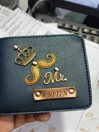 A very regal design. This blue leather wallet features a crown, a mustache, and 'Mr.' charms for 'Nitin'.