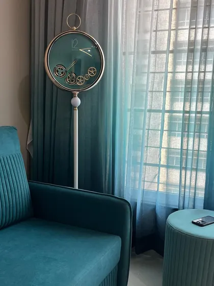 A closer look at the floor clock and the beautiful sheer curtains that filter natural light. The color coordination between the furniture and curtains creates a harmonious and well-designed interior.