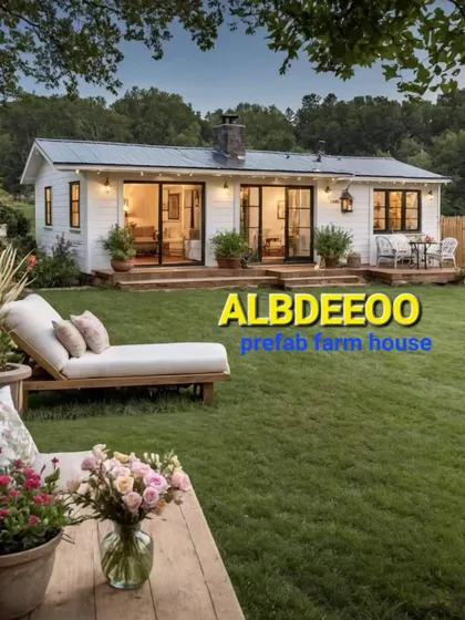 This image captures the dream of a modern prefab farmhouse. The structure features large glass doors that open up to a beautiful lawn, creating a seamless indoor-outdoor living experience.