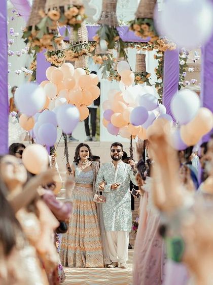 The couple's grand entrance at their carnival themed event in Udaipur. The balloons and cheering crowd create a festive and joyful atmosphere.