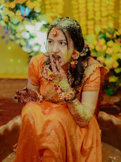 A fun and candid moment as the bride, covered in turmeric, enjoys a sweet treat during her Haldi ceremony.