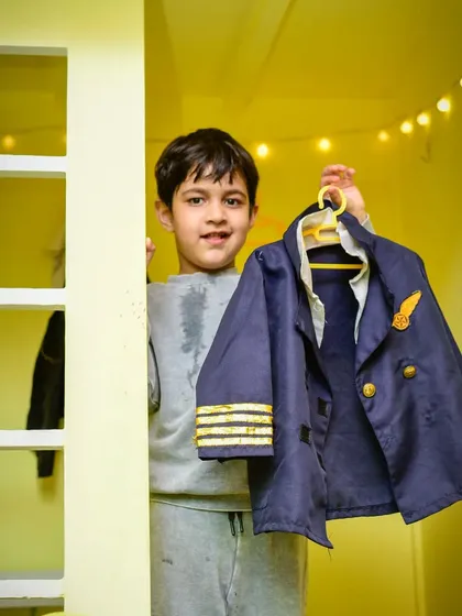 Ready for takeoff! A young boy proudly holds up his pilot jacket, excited to dress up and play.