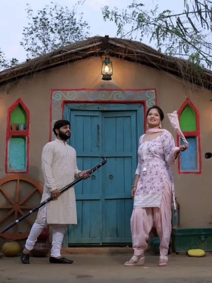 A fun and traditional pre-wedding shot with a rustic village hut backdrop. The couple's coordinated outfits and playful props make this a charming and unique photo.