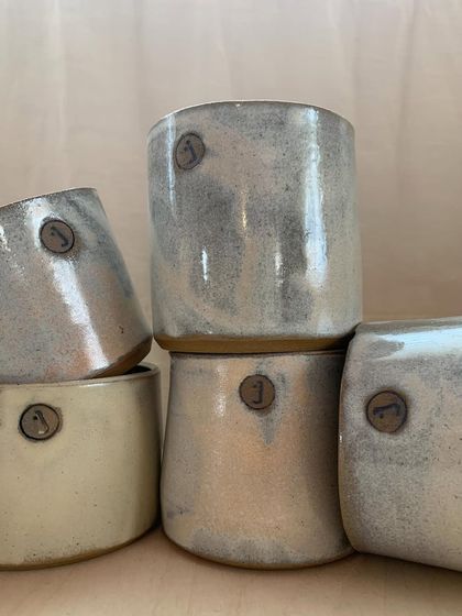 A close-up of the studio cups, showing the beautiful, rustic glaze and the custom stamp.
