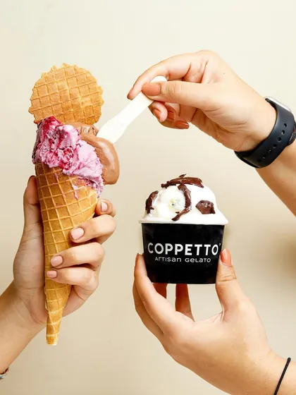 A playful interaction between two ways to enjoy gelato, a cone and a cup, showing the creamy texture of the dessert.