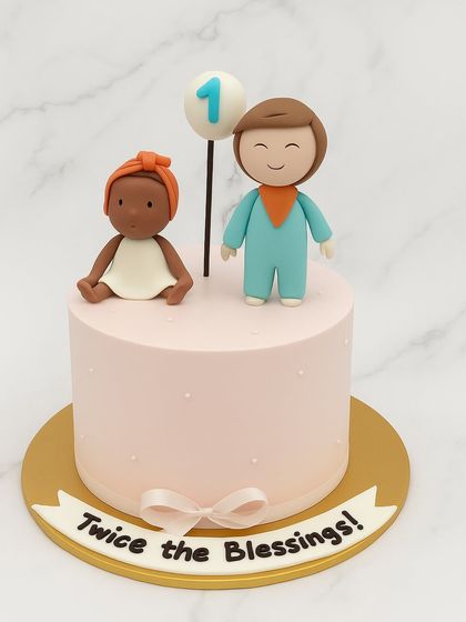 Celebrating twins is double the joy. This sweet pink cake is topped with custom fondant figurines representing the two little ones, complete with a "Twice the Blessings" banner.