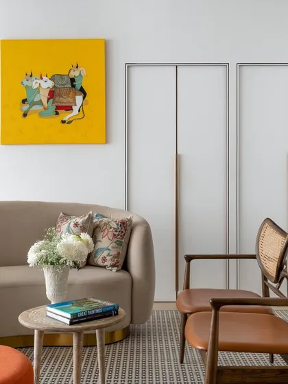 A closer view of the central lounge at Ra Clinic, where clients can unwind before their treatments. The neutral curved sofa, cane chairs, and patterned rug create a textured, comfortable setting. The vibrant yellow artwork, a piece from the client's personal collection, adds a joyful and personal touch to the space.
