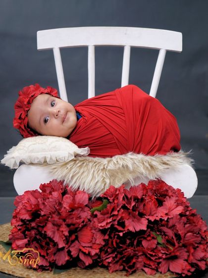 Another angle of this alert newborn. The simple setup with a white chair and red flowers keeps the focus entirely on her beautiful expression.