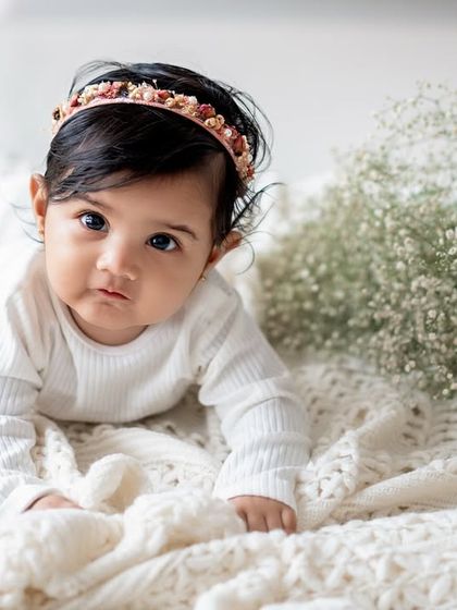 A baby girl lying on a soft blanket next to a bouquet of baby's breath.