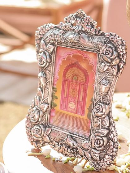 A small, ornate silver frame holding a Pichwai-style painting, used as a decorative accent on a side table.