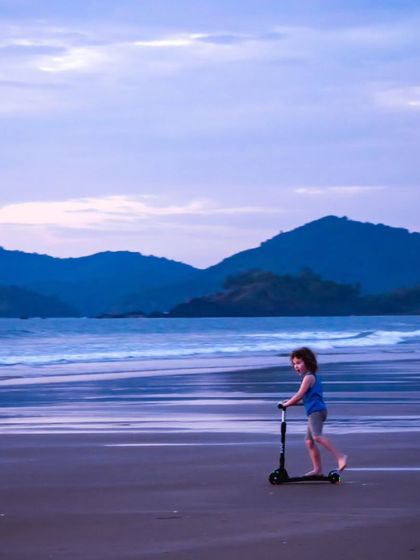 The simple joy of a child riding a scooter on the beach at dusk. The vastness of the sea and sky creates a beautiful sense of scale and freedom.
