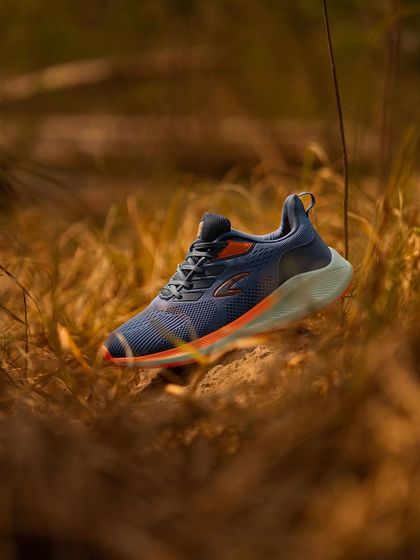 A single running shoe placed in a natural, grassy environment. The shallow depth of field makes the shoe the hero of the shot.