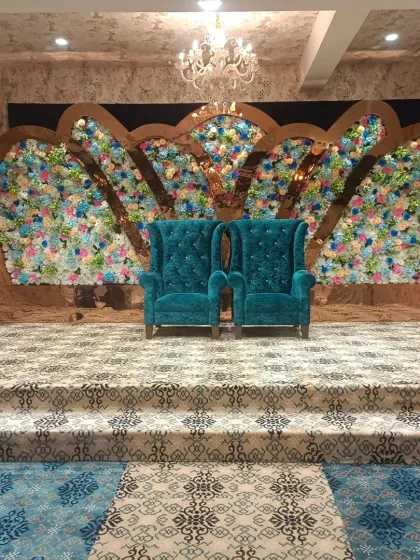 A grand reception stage with two high-back teal chairs set against a massive floral backdrop in the shape of wings. This bold design at Emerald Door banquet makes a powerful statement.