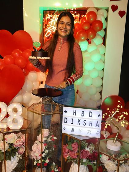 The birthday girl, Diksha, holds her cake, surrounded by red and white balloons and floral decor. Our custom lightboxes add a personal touch to every celebration.
