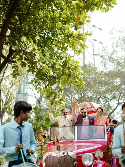 The couple's grand exit in a vintage car, surrounded by a marching band. A perfect, cinematic ending to their wedding celebration.